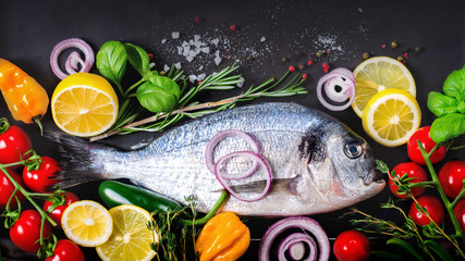 Fresh uncooked fish, dorado, sea bream with lemon, herbs, vegetables and spices on stone background. Top view. Banner