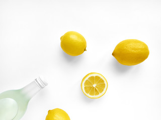 Lemonade in bottle Transparent glass bottle with lemonade, three whole lemons and one lemon's half are lying on white background Photo mockup in top view with copy space