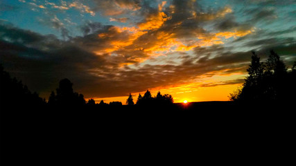 Dramatic red sunset / sunrise with cirrus clouds over rural field with silhouettes of forest trees and horizon line.