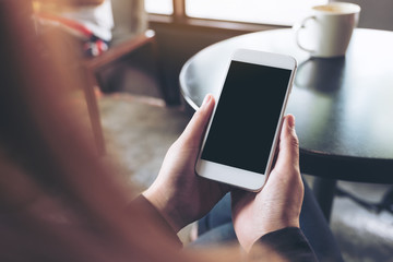 Mockup image of woman's hands holding white mobile phone with blank black desktop screen in cafe