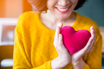 Woman  hands in yellow sweather holding pink heart.