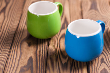Two colored empty ceramic clean mugs on old worn brown wooden table