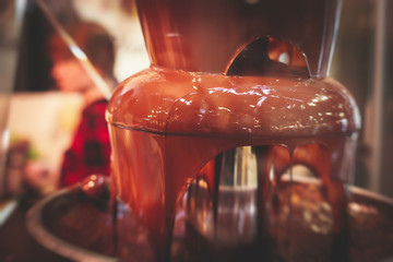 Vibrant Picture of Chocolate Fountain Fontain on childen kids birthday party with a kids playing around and marshmallows and fruits dip dipping into fountain
