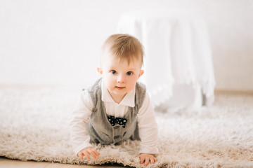 Fototapeta premium Cute happy kid in stylish gentleman suit crawling at home on light background