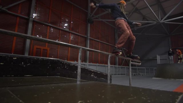 A couple of friends watch as a man with dreadlocks performs tricks on rollers