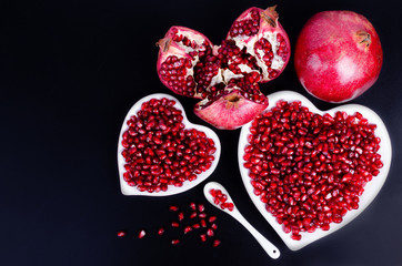 Two white heart shaped plates full of fresh juicy pomegranate seeds, little spoon, whole fruit and ripe one. Toned.