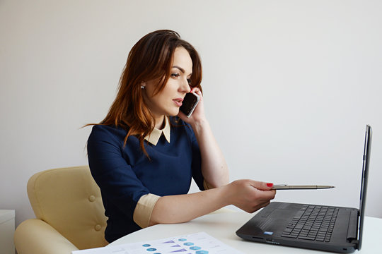  Attractive businesswoman working on laptop and making phone call - Powered by Adobe