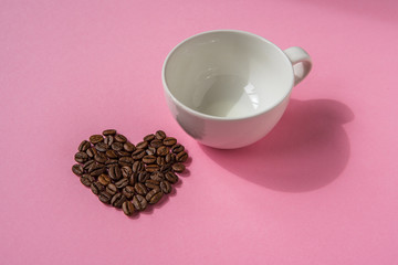 Coffee beans shaped hearts and white cup on a pink background. Love coffee concept