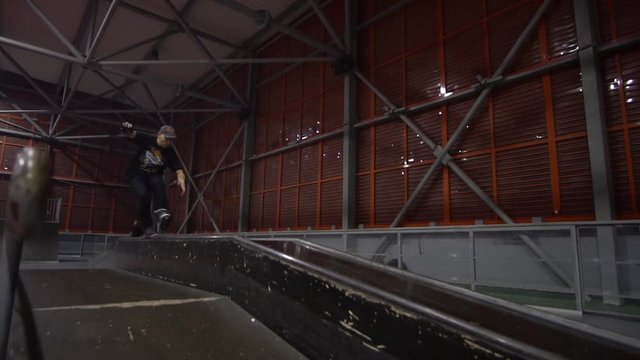 A man on rollers skates in a skate park and does extreme tricks, slow motion