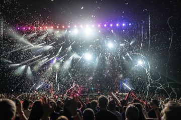 Silhouettes of people at the concert in front of the bright lights of the stage. Dark background, confetti, concert spotlights