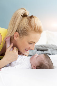 beautiful, young mother with yellow shirt with her baby in bed are cuddling and having fun