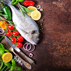Dorada, fresh fish with vegetable, lemon, herbs, onion, paprika, cherry tomatoes, onion, salton dark vintage background. Copy space.