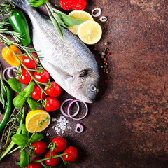 Fresh uncooked fish, dorado, sea bream with lemon, herbs, vegetables and spices on rustic background. Top view. Free space for your text