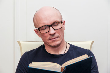 adult bald man in glasses reading a book