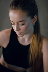 Close up portrait of a beautiful blonde girl with ponytail in black sportswear in the gym. Dark background.