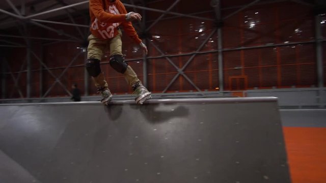 A man in an orange sweatshirt makes risky stunts on rollers, slow motion