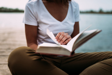 Close up of woman reading a book outdoors, next to the lake.