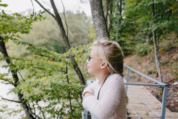 Portrait of a blonde girl with glasses outdoors in the park on the background of a wooden bridge