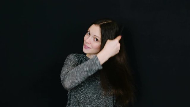 Smiling brunette woman looking at the camera and brushing her hair against a black background. Room for text.