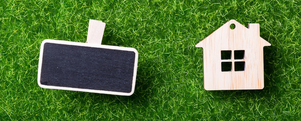 Model of wooden house and mockup board on green grass background
