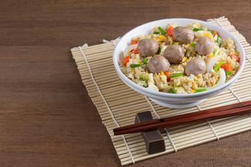 meatball and vegetable fried rice in a ceramic bowl with chopsticks and bamboo mat on wooden table, close up. homemade style healthy food concept.
