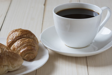 A cup of coffee, croisant and bread on wooden background