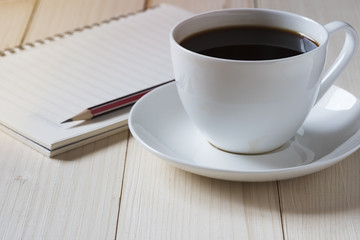 A cup of coffee and a notepad with pencil ontop