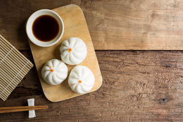 top view of steamed chinese bun (baozi) on cutting board served with soy sauce in rural kitchen, copy space for text. popular dim sum food menu.