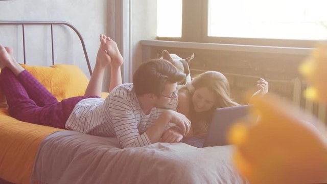 Happy young couple with french dog with laptop at home. Slow motion