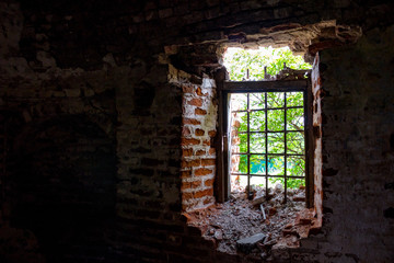 Broken window with wrought iron grating in the old abandoned 18th century building, inside view
