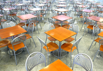 Many brown square eating tables and metal chairs staying in empty cafe hall inside high modern building