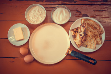Kitchen ingredients, pancakes and empty frying pan on rustic wooden background. Top view with copy space.