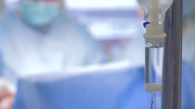 Close up of a full drip flask with a group of surgeons working in the background