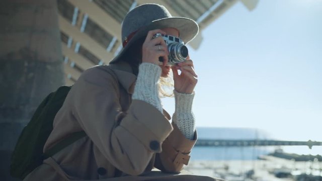 Young traveler woman in hat capturing moment on vintage film camera, stylish woman walking in the city enjoying her vacation in Europe, slow motion