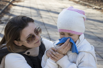 Child with runny nose. Mother helping to blow kid's nose with paper tissue. Seasonal sickness.