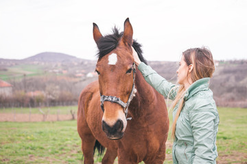 Beautiful young woman on the ranch bonding with a brown horse.
