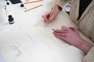 Calligraphy lettering workshop. Young women's hand, writting letters. Calligraphy sheets, nibs, paper, ink and pens