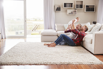 Young white couple play with their toddler in sitting room