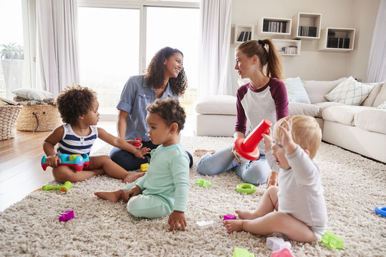 Two friends playing with toddler kids on sitting room floor