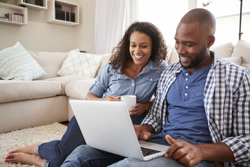 Young black couple using laptop sitting on the floor at home