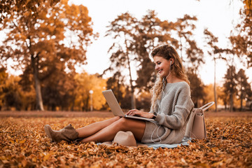 Side view of beautiful girl with curly hair using laptop in the autumn park.