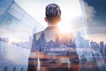 The double exposure image of the businessman standing back during sunrise overlay with cityscape image. The concept of modern life, business, city life and internet of things. - obrazy, fototapety, plakaty