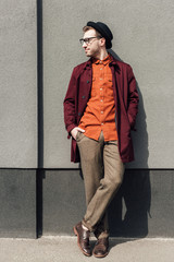 handsome stylish man in trendy hat standing at grey wall