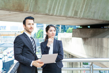 Fototapeta premium Young business Man and woman working together on a laptop outdoors in modern city. Portrait of a woman and a man in front of a laptop computer. Boss working on a building site holding a laptop.