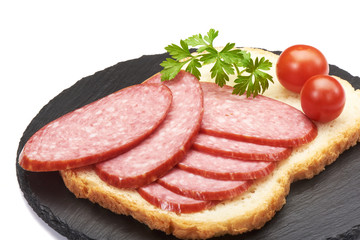 Tasty appetizer of thinly sliced spicy salami on wholewheat bread with a seed crust and liberal spread of butter or margarine topped with parsley, on a stone rustic board isolated on white background