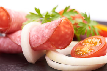 Tasty appetizer of thinly sliced spicy salami smoked sausage whith colorfull vegetabless on a stone rustic board isolated on white background