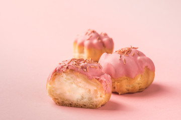 Fresh air dessert profiteroles with a delicate cream decorated with pink glaze. Isolated on a pink background.