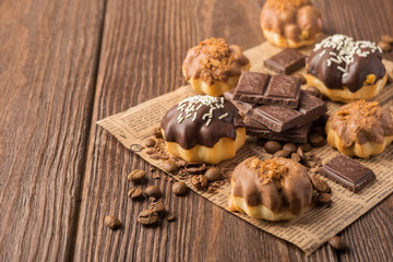 Fresh air dessert chocolate profiterole with a delicate cream decorated with a glaze of milk and dark chocolate on a dark wooden background.