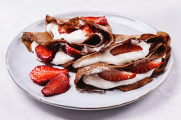 Homemade chocolate crepes with strawberry and cream on grey concrete background. Delicious breakfast. Selective focus