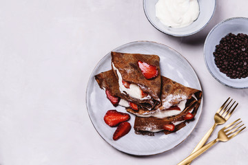 Homemade chocolate crepes with strawberry and cream on grey concrete background. Delicious breakfast. Selective focus